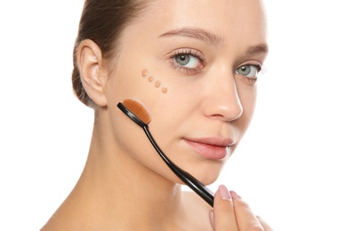 Young woman applying foundation on her face against white background