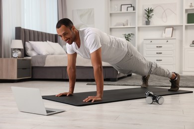 Man doing morning exercise on fitness mat near laptop at home