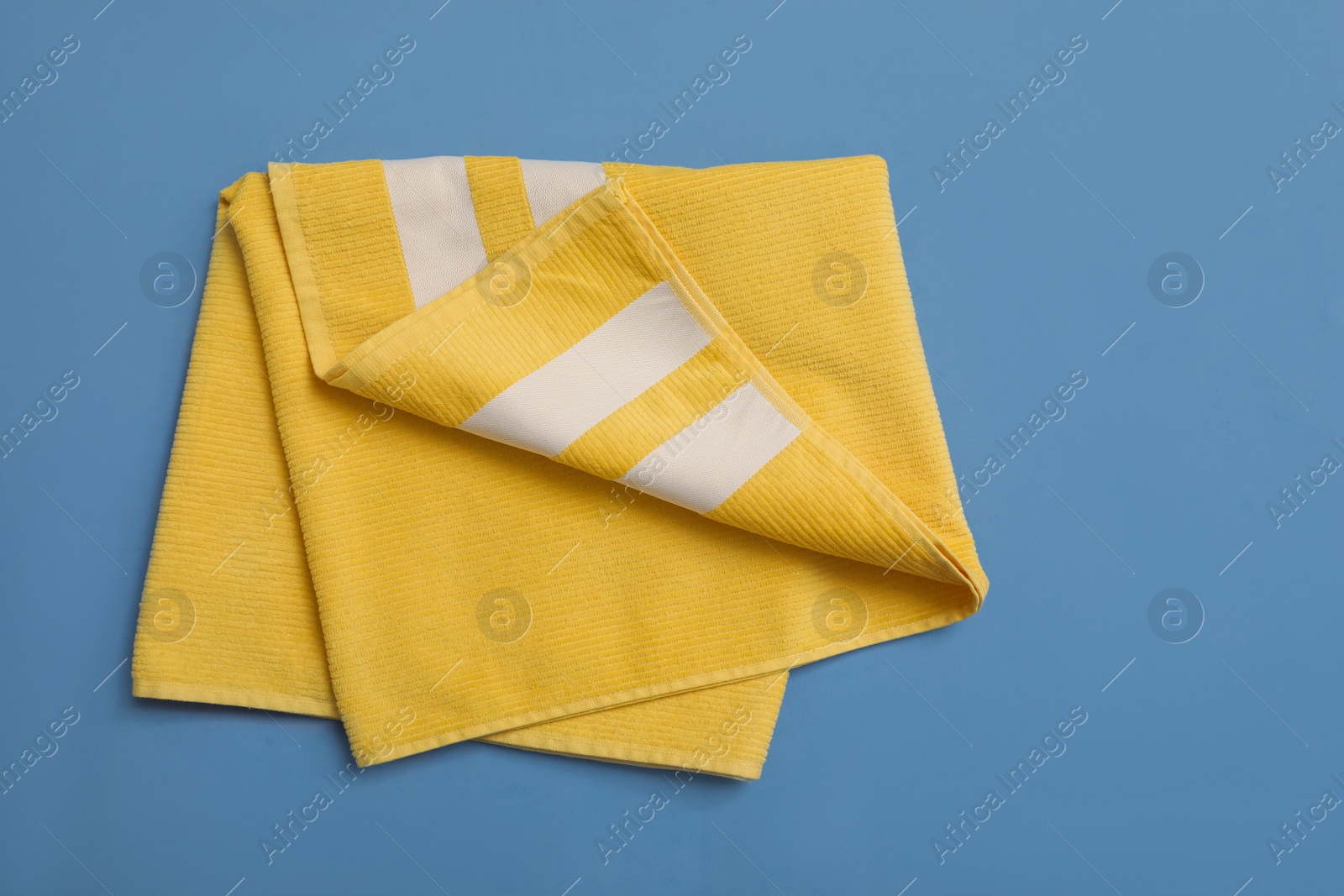 Photo of Folded yellow beach towel on blue background, top view