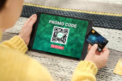 Image of Woman holding credit card and tablet with activated promo code in online shopping app at wooden table, closeup