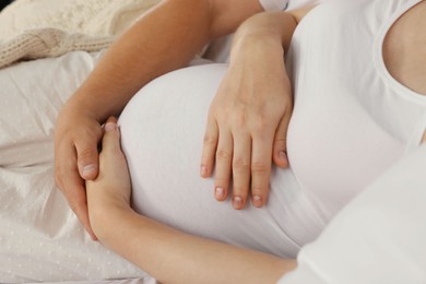 Photo of Man hugging his pregnant wife on bed, closeup