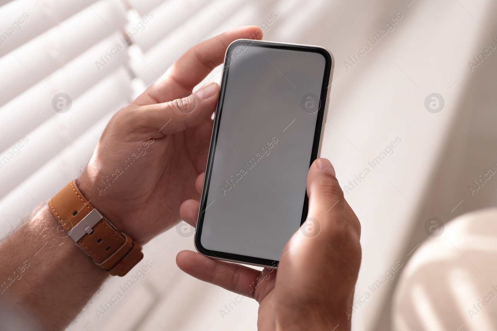 Photo of Man holding mobile phone with empty screen near window indoors, closeup