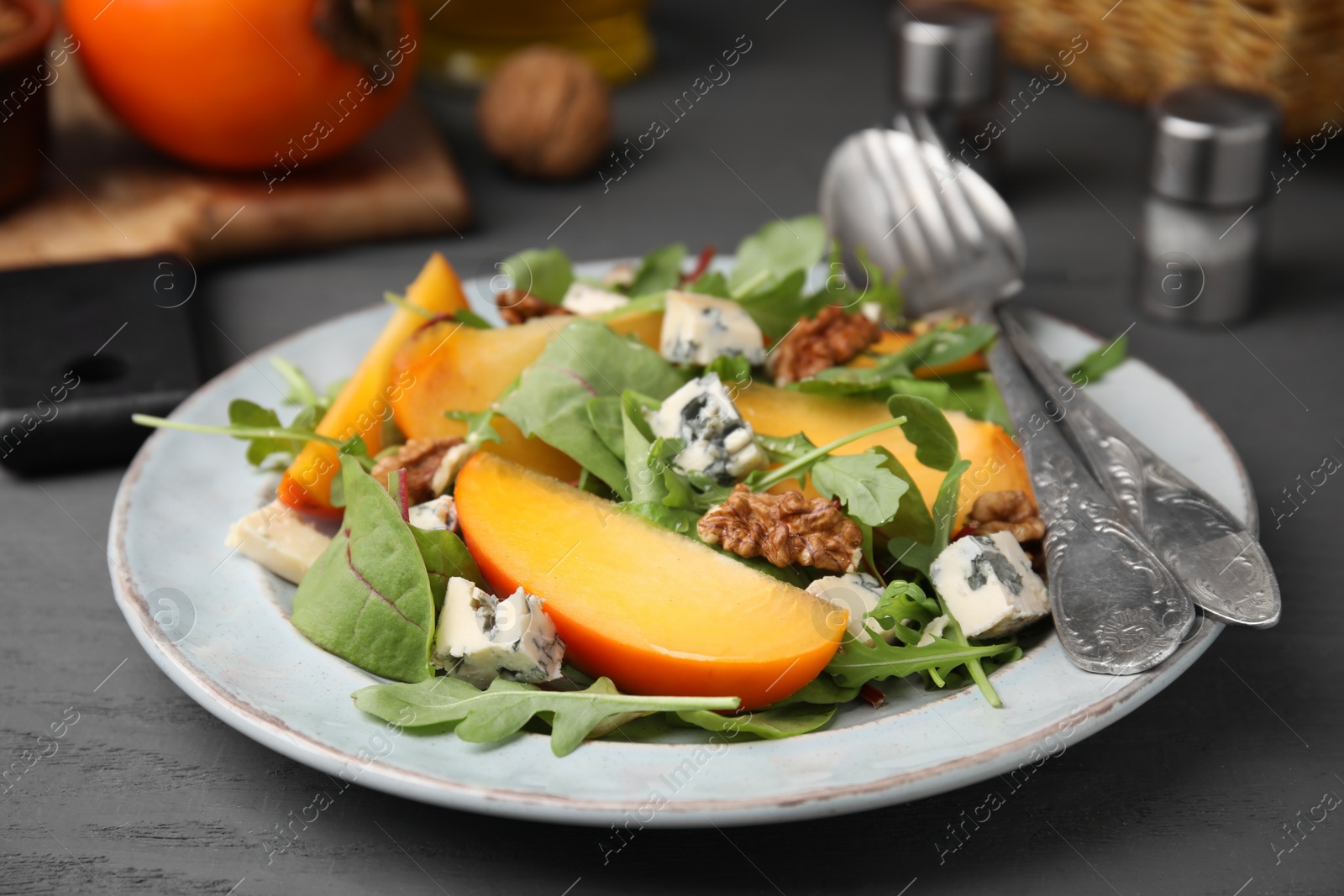 Photo of Tasty salad with persimmon, blue cheese and walnuts served on grey wooden table, closeup