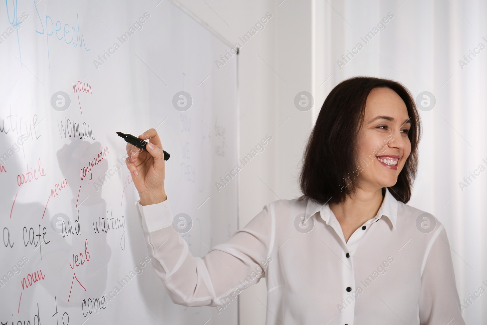 Photo of English teacher giving lesson near whiteboard in classroom