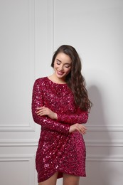 Photo of Beautiful young woman in stylish pink sequin dress near white wall indoors. Party outfit