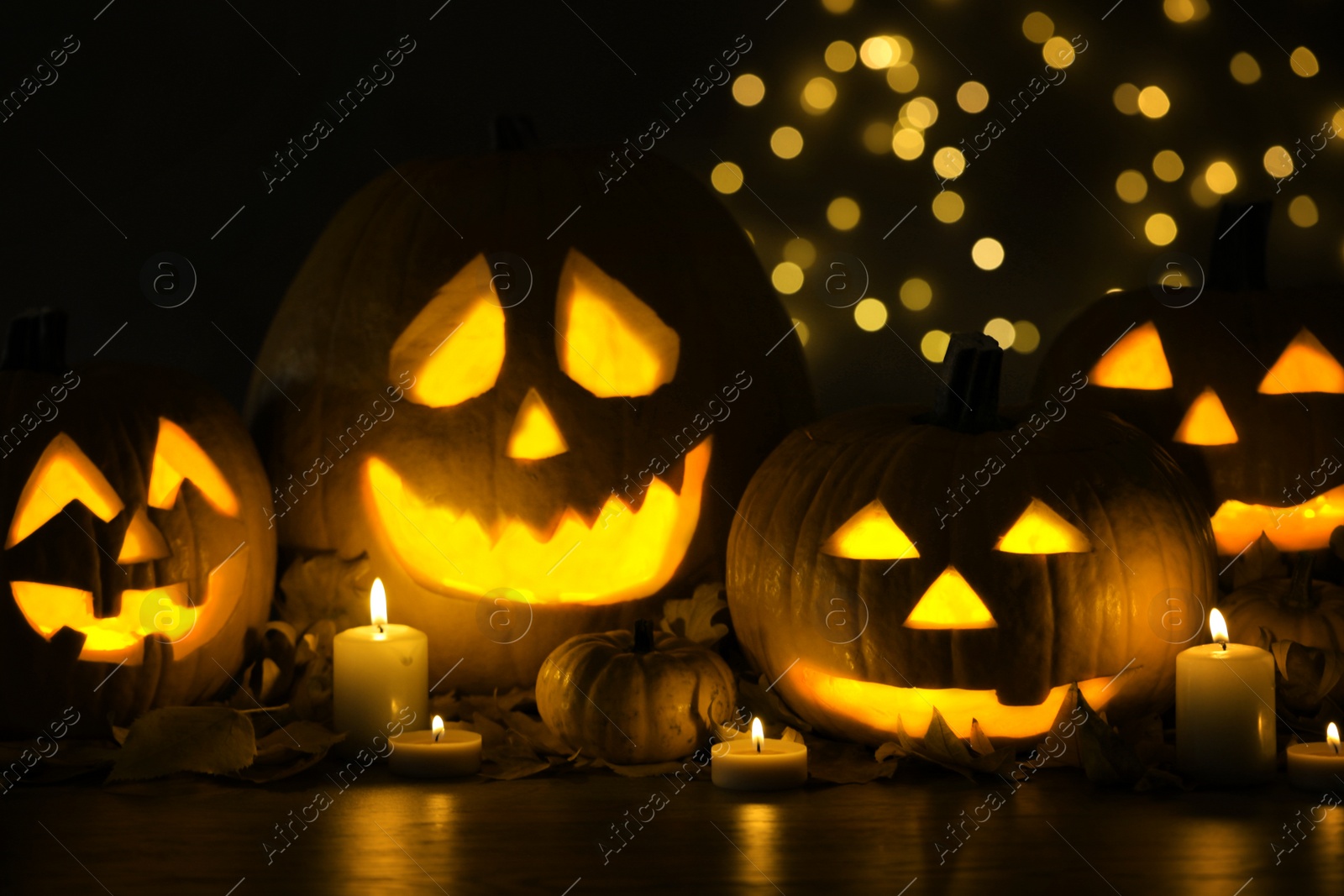 Photo of Pumpkin jack o'lanterns, autumn leaves and candles on table against blurred background. Halloween decor