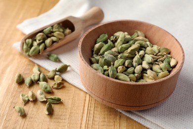 Photo of Bowl and scoop of dry cardamom pods on wooden table