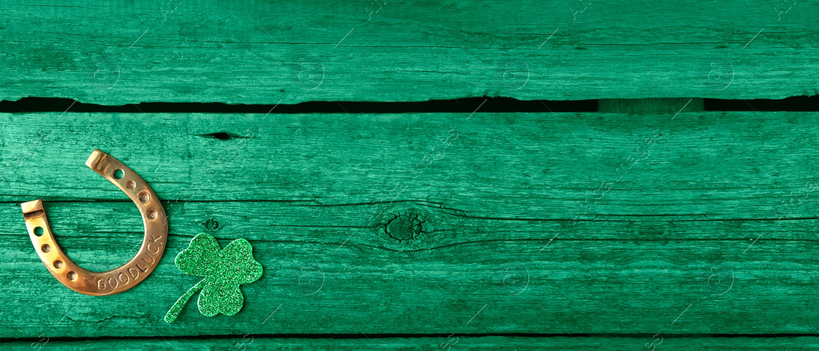 Image of St. Patrick's day. Decorative clover leaf and golden horseshoe on green wooden background, flat lay. Banner design with space for text