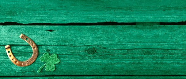 St. Patrick's day. Decorative clover leaf and golden horseshoe on green wooden background, flat lay. Banner design with space for text