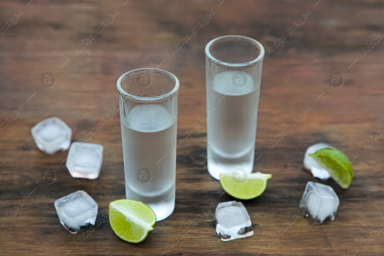 Photo of Mexican tequila shots with lime slices and ice cubes on wooden table. Drink made from agave