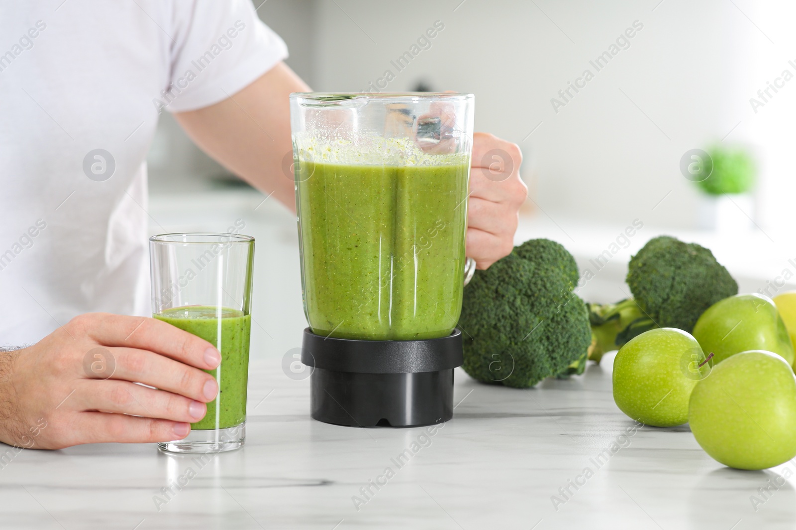 Photo of Man pouring delicious smoothie into glass at white marble table, closeup