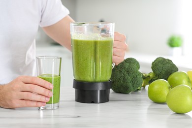 Man pouring delicious smoothie into glass at white marble table, closeup