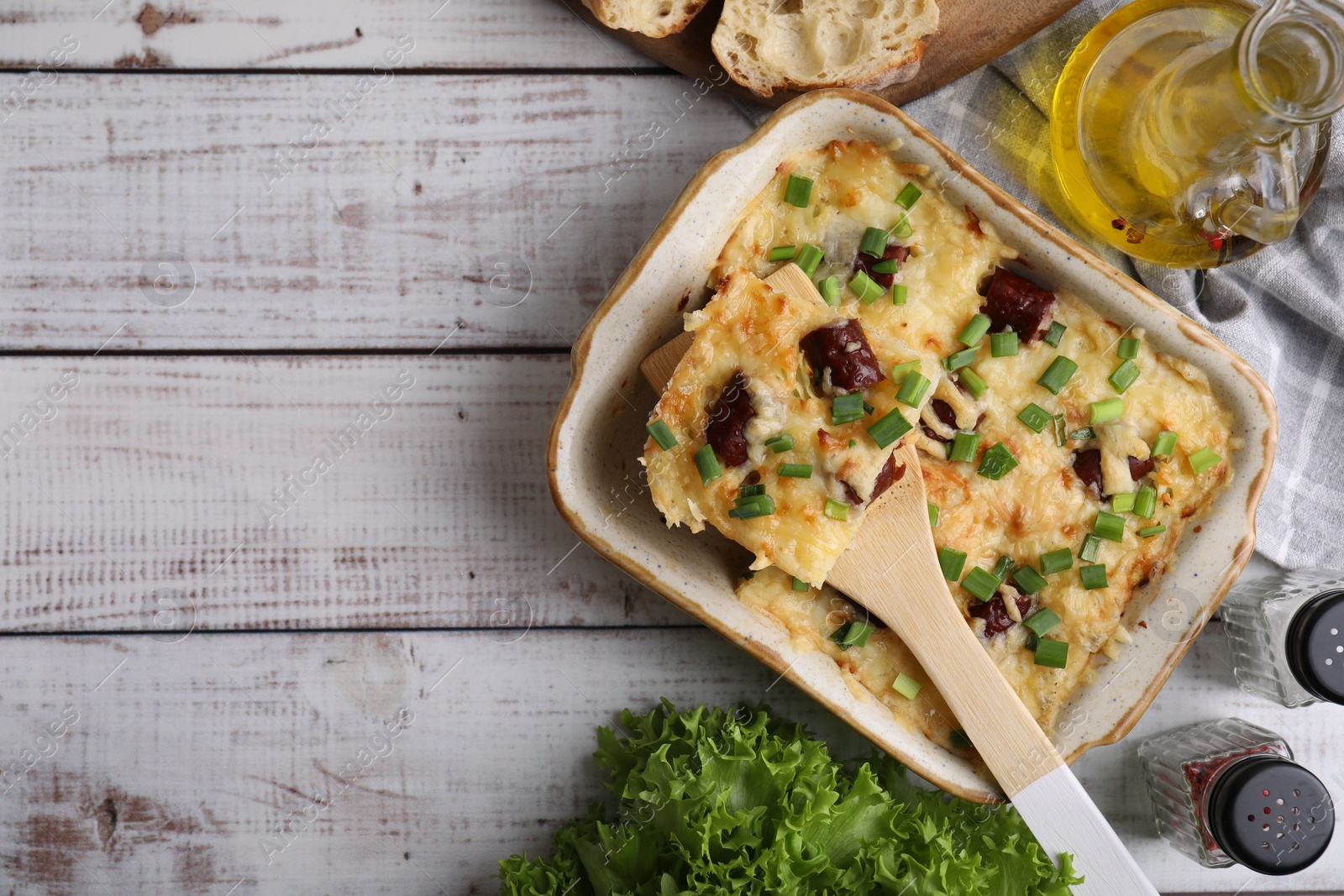 Photo of Tasty sausage casserole in baking dish served on white wooden table, flat lay. Space for text