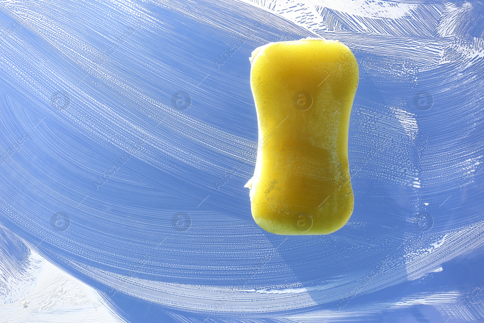 Photo of Sponge and cleaning foam on glass, closeup