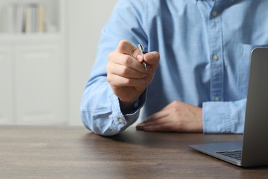 Photo of Man with pen and laptop at wooden table, closeup. Space for text
