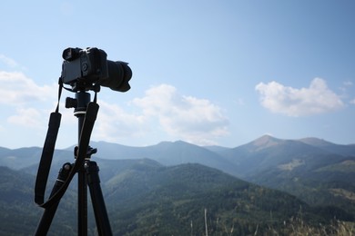 Photo of Tripod with modern camera in mountains on sunny day. Professional photography