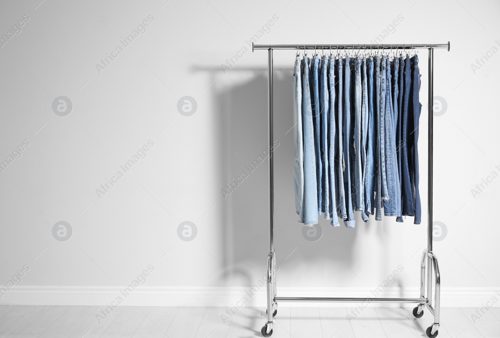 Photo of Rack with different jeans near light wall. Space for text
