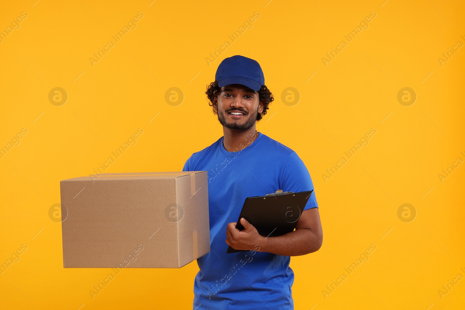 Photo of Happy courier with parcel and clipboard on orange background