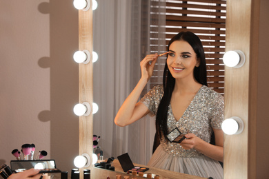 Beautiful young woman applying makeup near mirror in dressing room