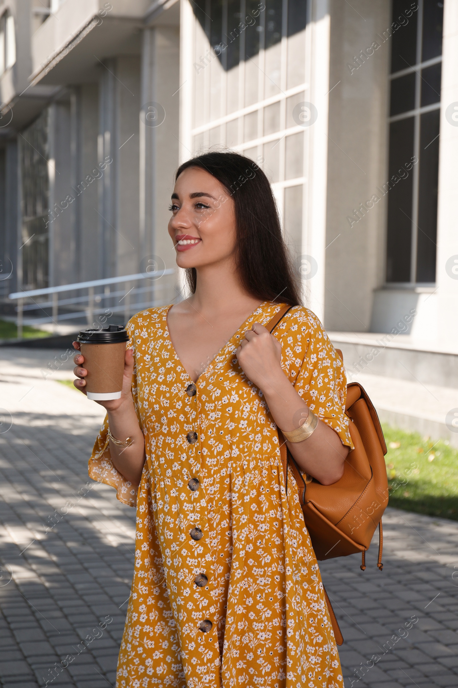 Photo of Beautiful young woman with stylish backpack and cup of coffee on city street