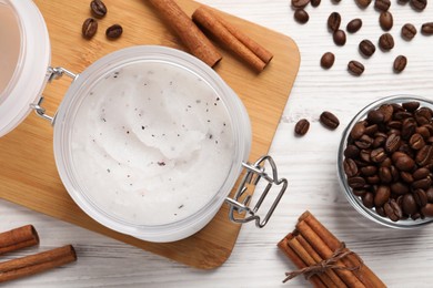 Body scrub in glass jar, cinnamon and coffee beans on white wooden table, flat lay