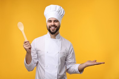 Photo of Happy young chef in uniform holding wooden spoon on orange background