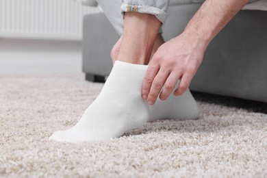 Photo of Man putting on white socks at home, closeup