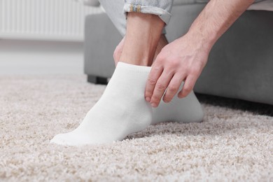 Man putting on white socks at home, closeup