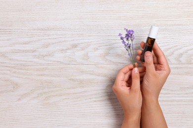 Photo of Woman with bottle of lavender essential oil and flowers on wooden background, top view. Space for text