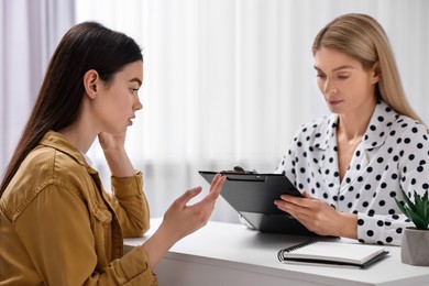 Psychologist holding clipboard while working with teenage girl at table in office