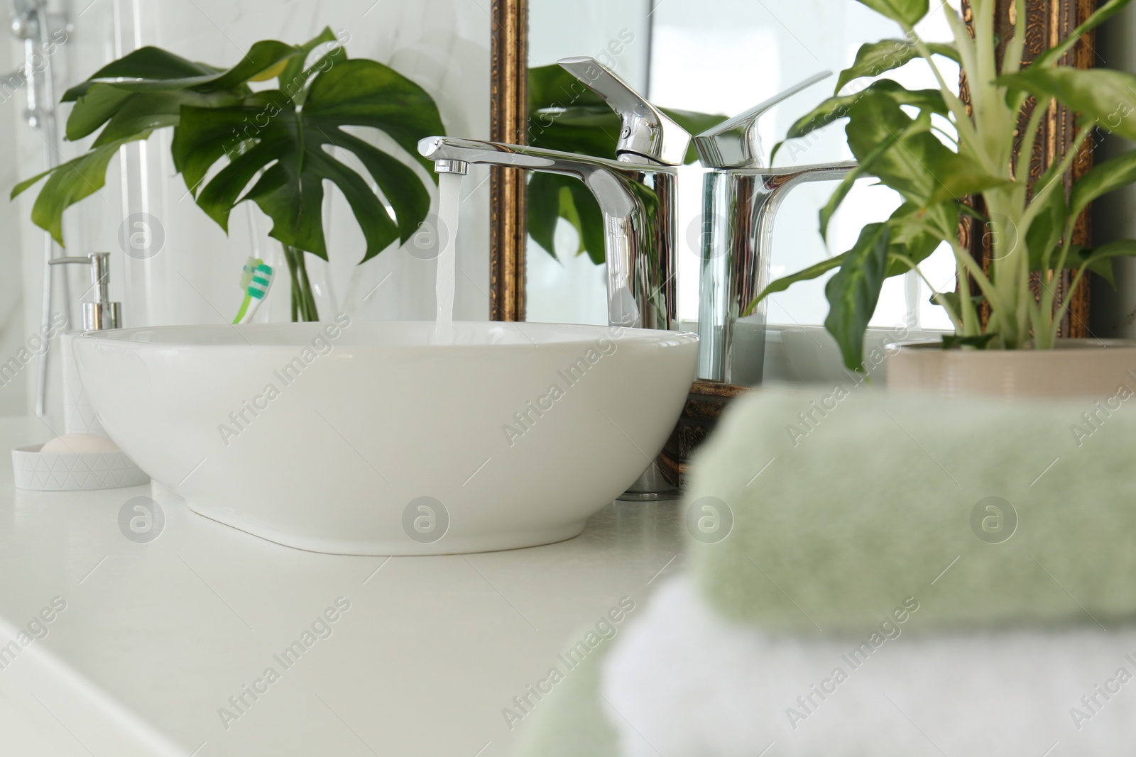 Photo of Water running from faucet into sink near mirror in bathroom