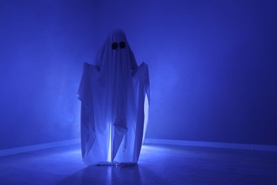Photo of Creepy ghost. Woman covered with sheet in blue light, space for text