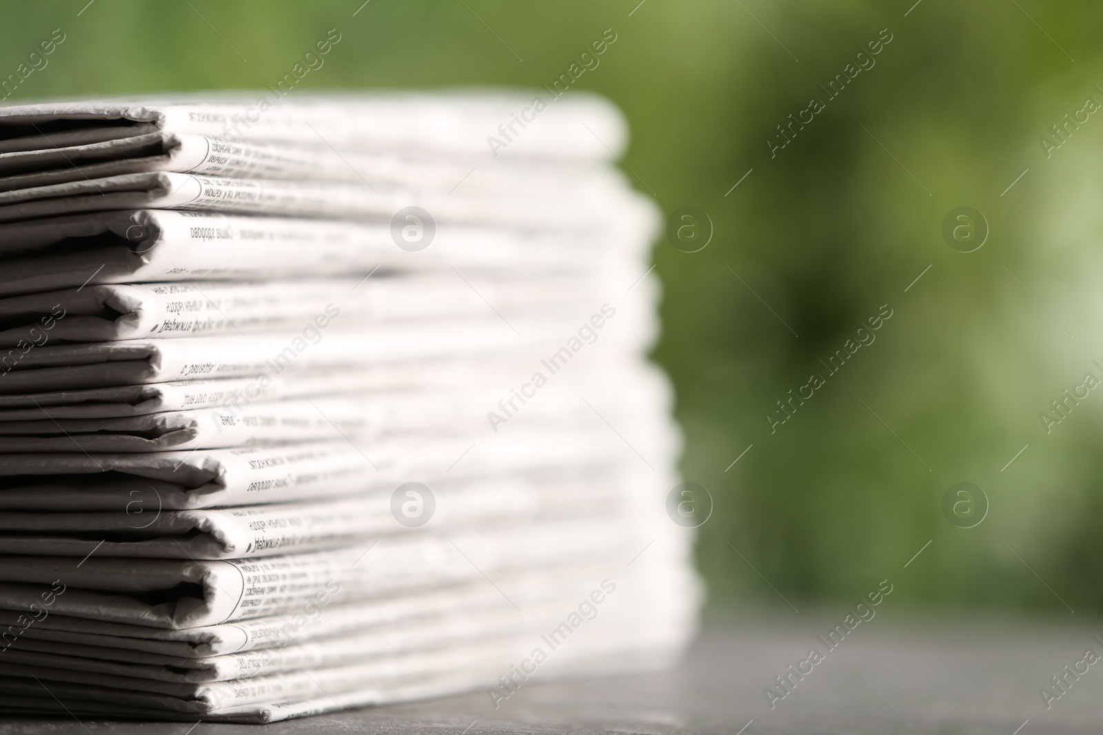 Photo of Stack of newspapers on grey table against blurred green background, closeup. Journalist's work