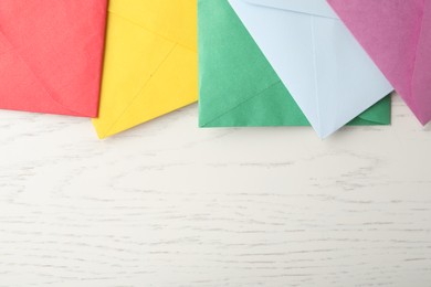 Colorful paper envelopes on white wooden background, flat lay. Space for text