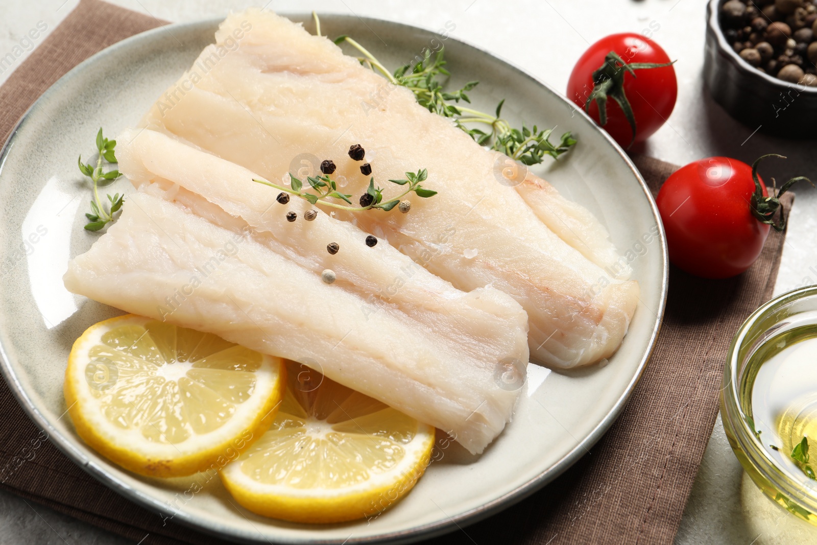 Photo of Plate with raw cod fish, spices, microgreens and lemon on table, closeup