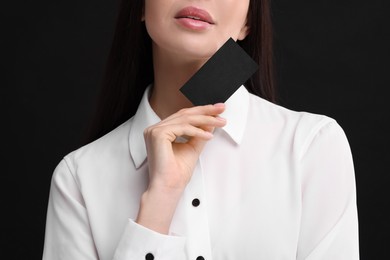 Woman holding blank business card on black background, closeup. Space for text