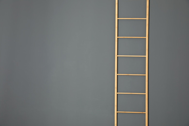 Photo of Modern wooden ladder on grey background. Space for text