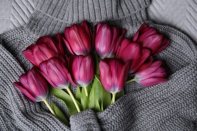 Photo of Beautiful purple tulips wrapped in gray sweater, top view