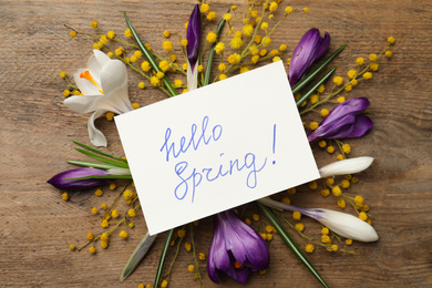 Photo of Card with words HELLO SPRING and fresh flowers on wooden table, flat lay