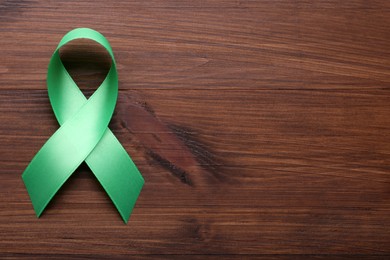 Photo of World Mental Health Day. Green ribbon on wooden background, top view with space for text