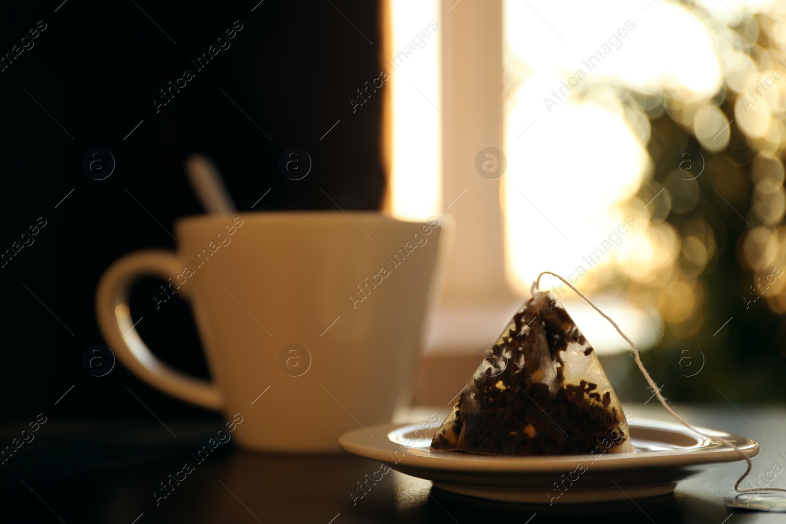 Photo of Saucer with used pyramid tea bag on table. Space for text