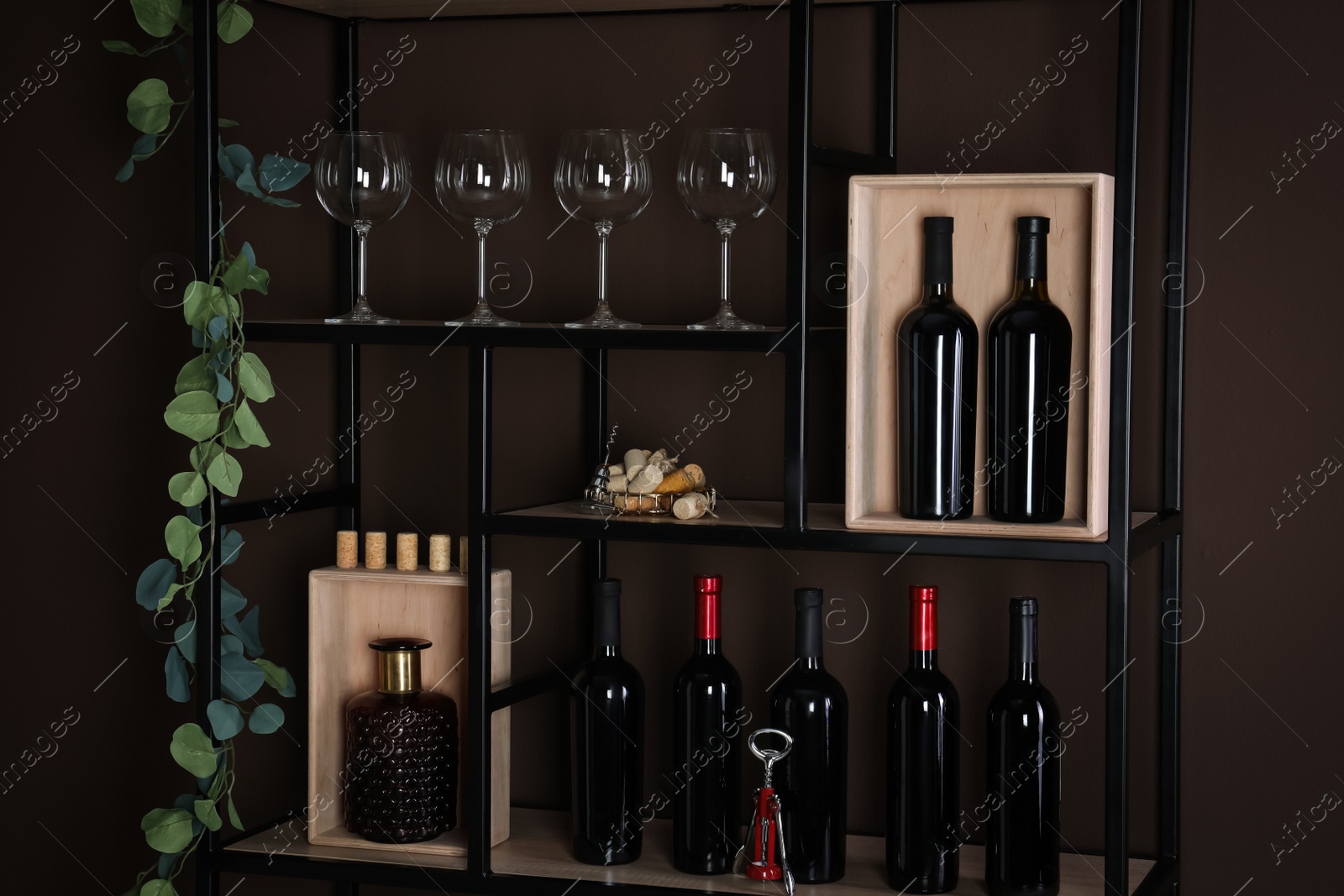 Photo of Rack with bottles of wine and glasses near brown wall