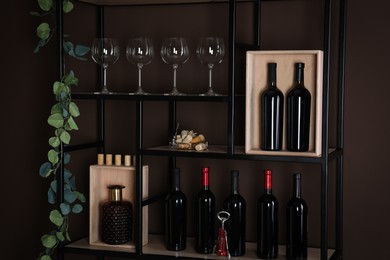 Photo of Rack with bottles of wine and glasses near brown wall