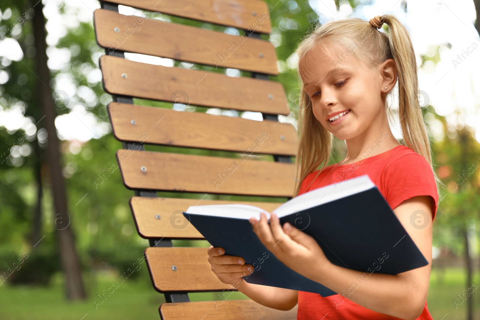 Image of Happy little girl reading book in park 