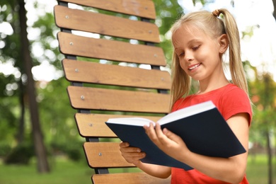 Happy little girl reading book in park 