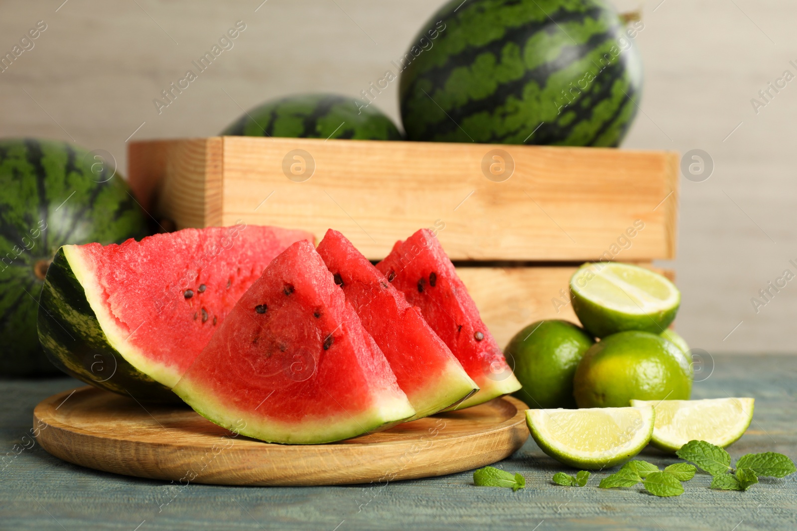 Photo of Slices of delicious watermelon, limes and mint on light blue wooden table