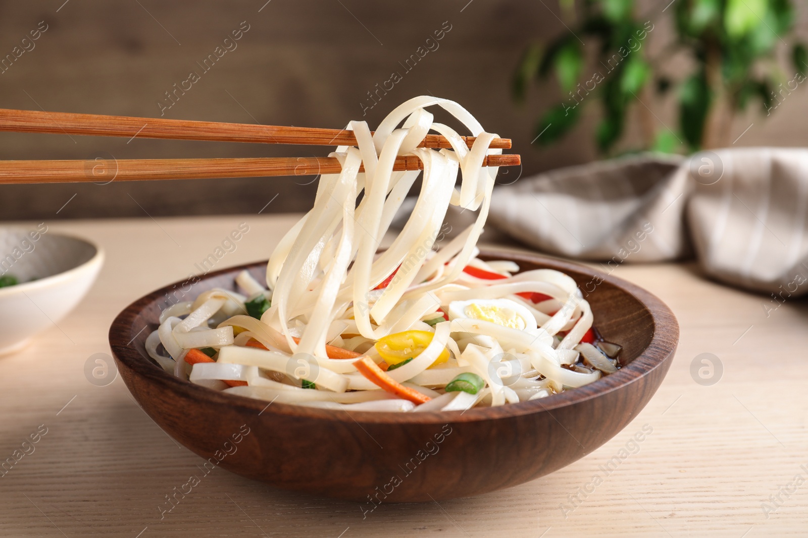 Photo of Chopsticks with asian noodles over bowl on wooden table