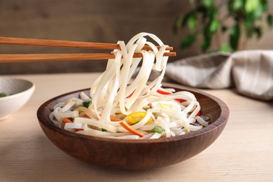 Chopsticks with asian noodles over bowl on wooden table