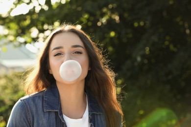 Photo of Beautiful young woman blowing bubble gum in park. Space for text