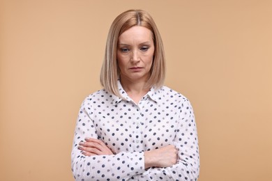 Portrait of sad woman with crossed arms on beige background